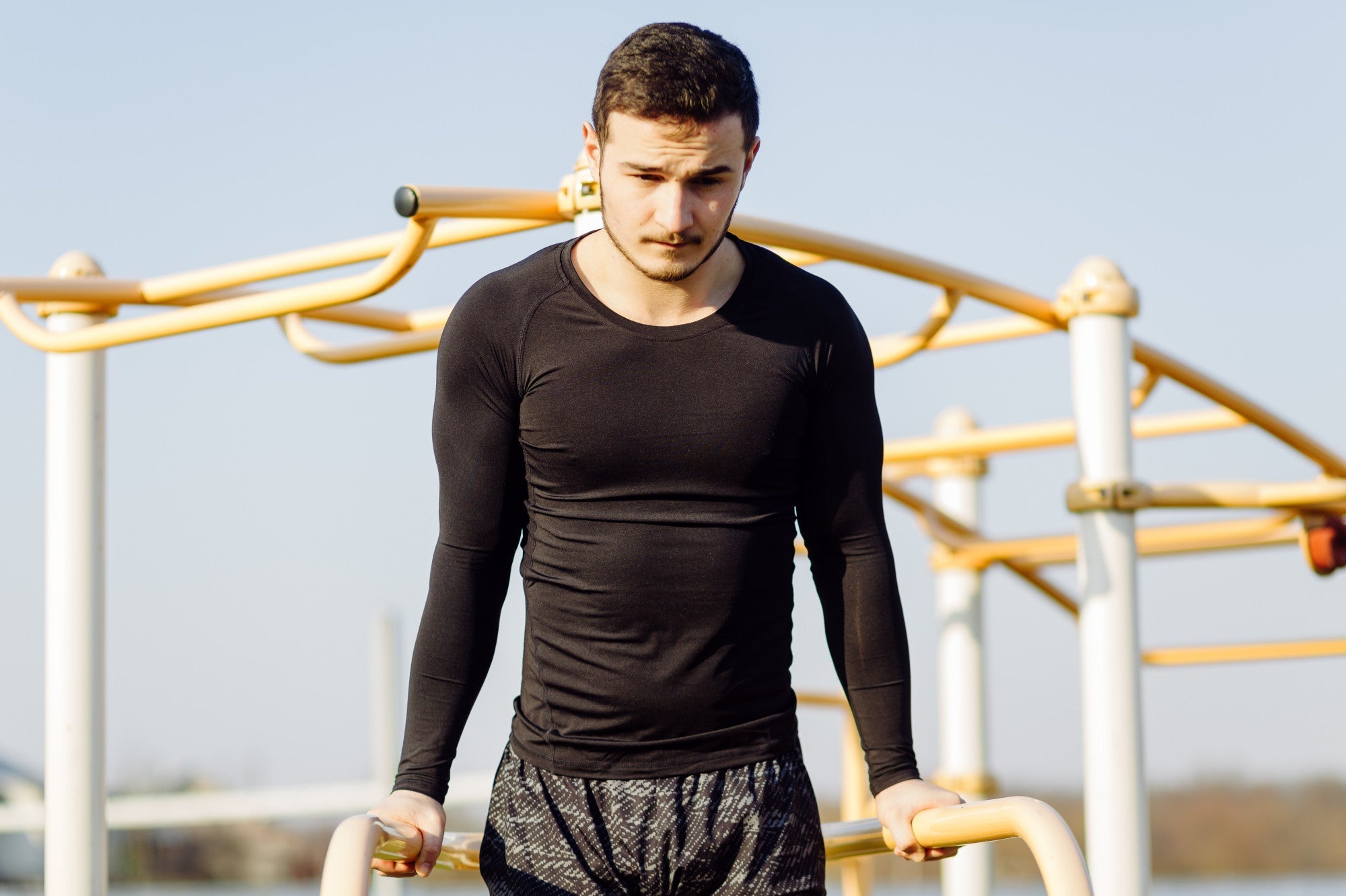 Man wearing a black long-sleeve compression top during an outdoor workout on parallel bars, men’s compression shirt