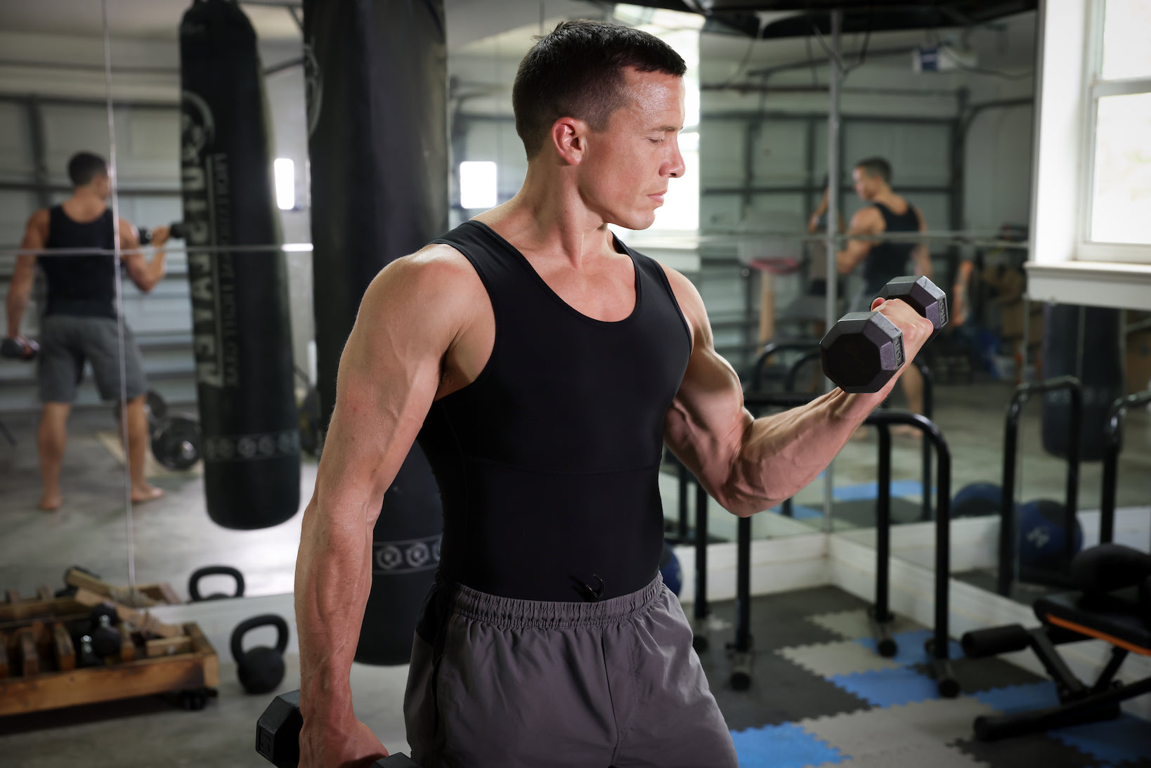 Man lifting dumbbells in a black compression tank during a gym workout, men’s shapewear shirt