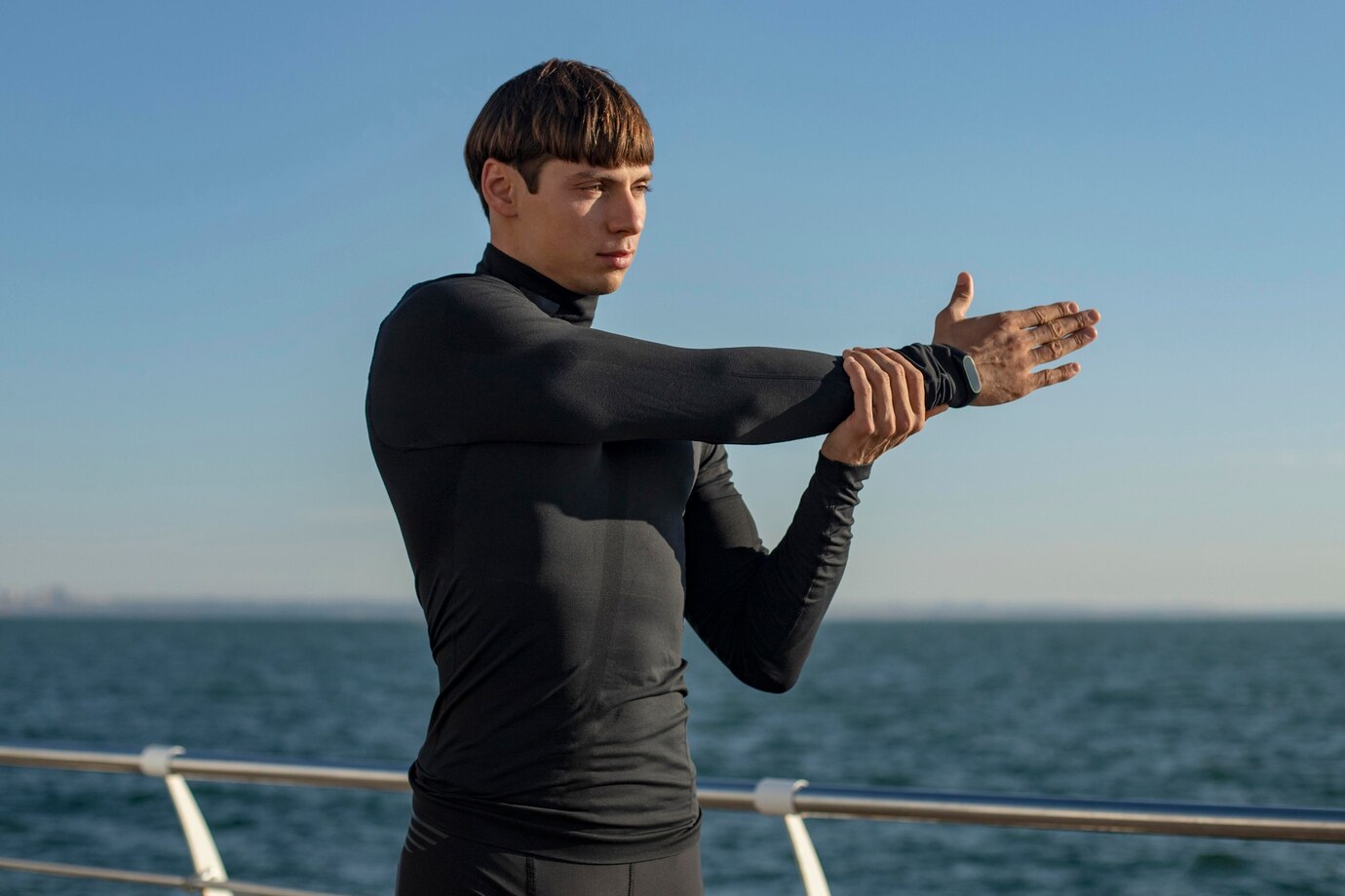 Man stretching in a black long-sleeve compression top by the water, men’s compression shirt